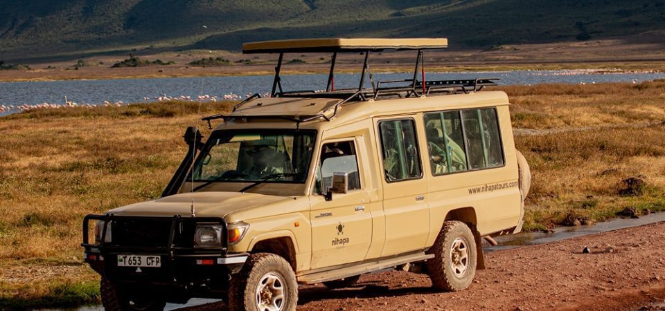A 4x4 safari vehicle parked on a rugged trail with a scenic lake and mountains in the background, showcasing a 2 Days Tanzania Safari adventure in Tarangire National Park and Ngorongoro Crater.