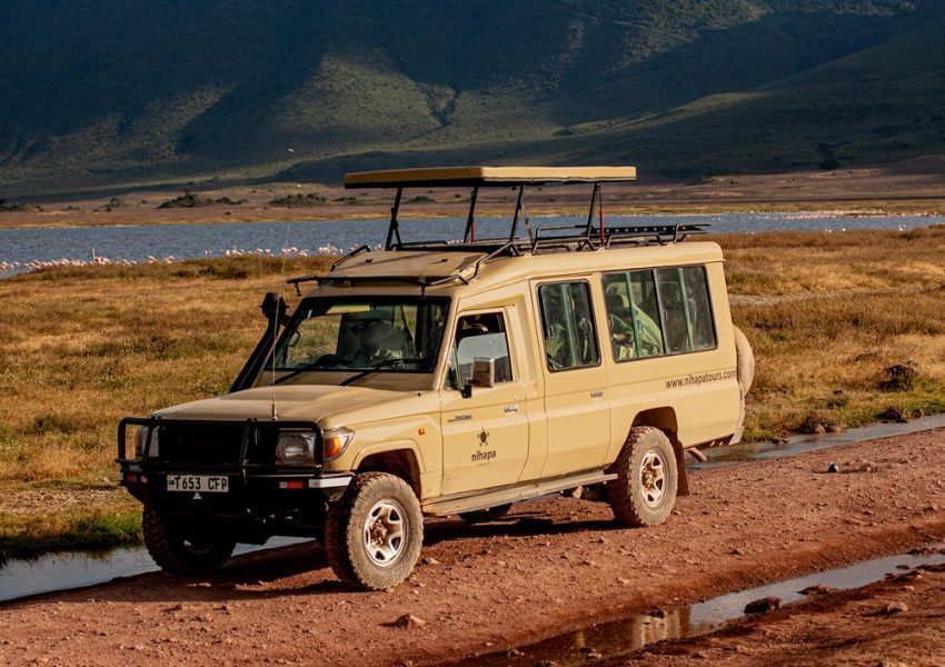 A 4x4 safari vehicle parked on a rugged trail with a scenic lake and mountains in the background, showcasing a 2 Days Tanzania Safari adventure in Tarangire National Park and Ngorongoro Crater.