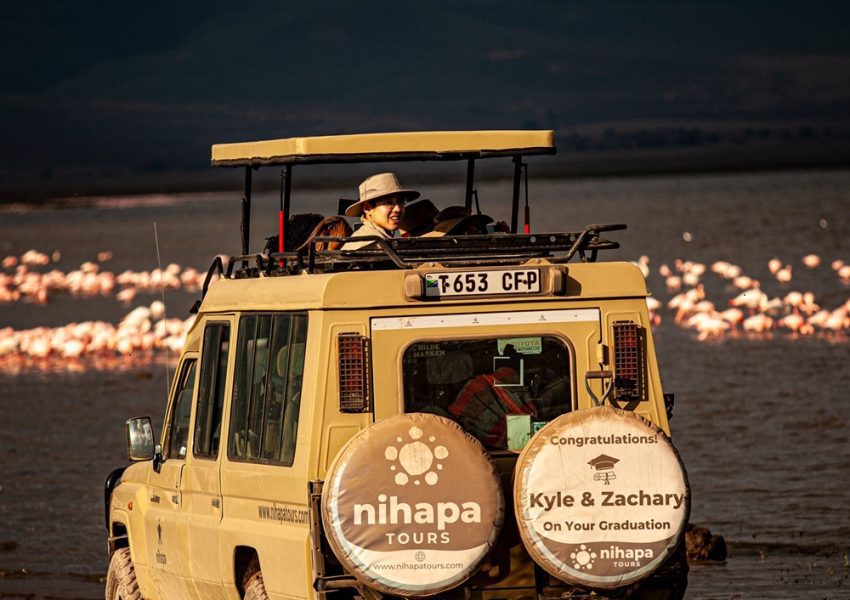 A Nihapa Tours safari vehicle on a 4 days Tanzania tour, parked near a lake with flamingos in the background, showcasing a luxury wildlife adventure in Tarangire, Serengeti, and Ngorongoro Crater.