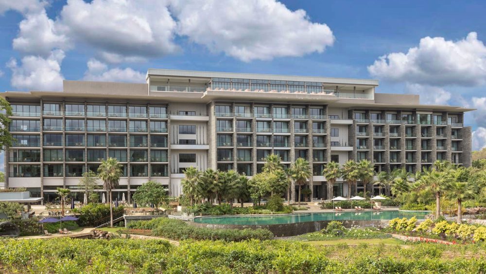 Luxurious Gran Melia Arusha Hotel with modern architecture, featuring multiple floors, balconies, and a serene pool surrounded by lush gardens and palm trees, ideal for Tanzania safari accommodation.