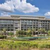 Luxurious Gran Melia Arusha Hotel with modern architecture, featuring multiple floors, balconies, and a serene pool surrounded by lush gardens and palm trees, ideal for Tanzania safari accommodation.