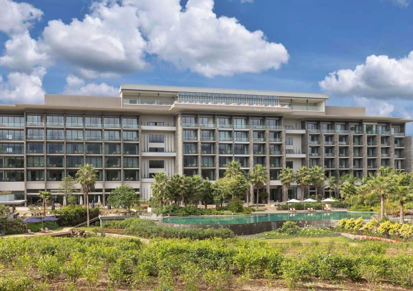 Luxurious Gran Melia Arusha Hotel with modern architecture, featuring multiple floors, balconies, and a serene pool surrounded by lush gardens and palm trees, ideal for Tanzania safari accommodation.